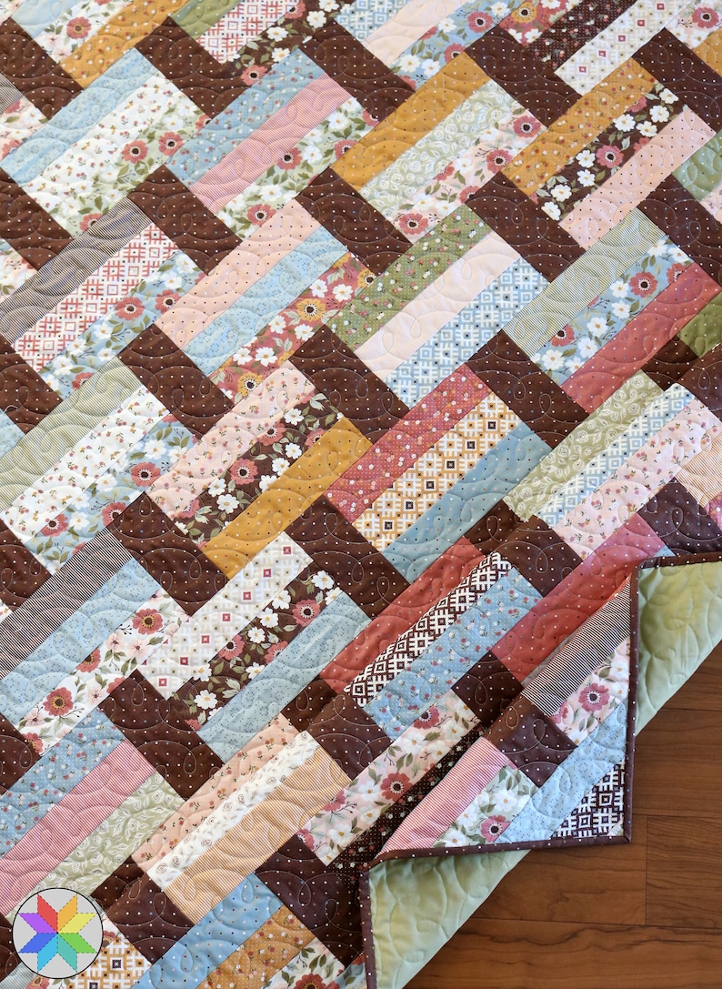 May include: A quilt with a brown, blue, pink, and green chevron pattern. The quilt is made of various floral and geometric patterned fabrics.