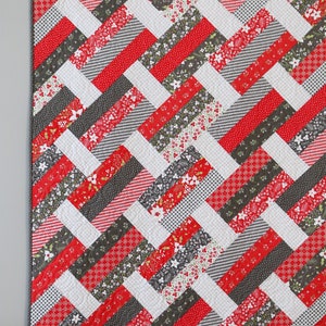 May include: A red, white, and gray quilt with a herringbone pattern. The quilt is made of various fabrics with different patterns, including floral, plaid, and polka dots.