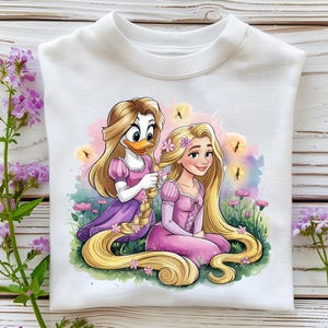 Pode incluir: Camisola branca de gola redonda com uma ilustração colorida de duas personagens de desenhos animados. Uma personagem, que se assemelha a um pato, trança o longo cabelo loiro de uma princesa. A princesa usa um vestido rosa e flores no cabelo. O fundo inclui flores e borboletas.