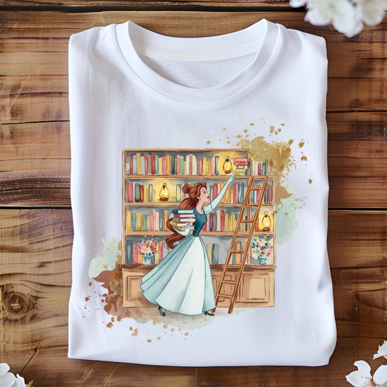May include: White t-shirt featuring a watercolor illustration of a woman in a blue dress reaching for books on a bookshelf. The design includes a wooden ladder, books, and a floral arrangement. The background has gold paint splatters.