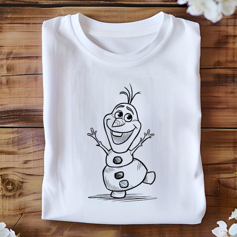 May include: White t-shirt featuring a black and white cartoon illustration of Olaf, the snowman character from the movie Frozen. Olaf is depicted with his arms raised and a cheerful expression. The t-shirt is folded neatly on a wooden surface.