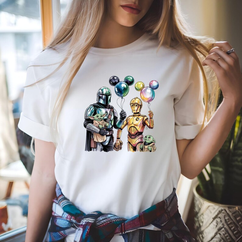 May include: White t-shirt featuring a graphic of characters from a science fiction franchise. The design includes a character in silver armor holding a small creature, a golden robot, and colorful balloons. The shirt is made of a soft material.