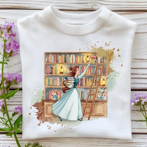 May include: White sweatshirt featuring a watercolor illustration of a woman in a blue dress reaching for books on a bookshelf. The design includes a wooden ladder, lanterns, and a floral arrangement, with brown and gold accents.