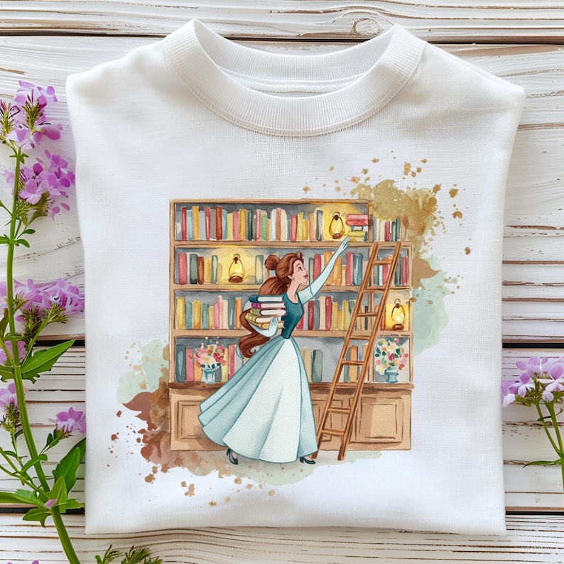 May include: White sweatshirt featuring a watercolor illustration of a woman in a blue dress reaching for books on a bookshelf. The design includes a wooden ladder, lanterns, and a floral arrangement, with brown and gold accents.