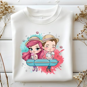 May include: White sweatshirt featuring a cartoon couple with pink and brown hair, wearing hats and holding drinks. They are seated on a blue bench against a backdrop of pink and teal watercolor splashes. Seashells and swirls decorate the design.