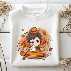 Puede incluir: Sudadera blanca con una ilustración de dibujos animados de una persona con sombrero y sosteniendo una porción de tarta de calabaza con crema batida. El diseño incluye hojas de otoño y una pequeña calabaza.