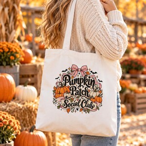 Könnte beinhalten: Eine weiße Stofftasche aus Segeltuch mit einem bunten Grafikdruck, der die Aufschrift Pumpkin Patch Social Club in schwarzer Schrift zeigt, umgeben von orangefarbenen Kürbissen, Herbstblättern, kleinen Fledermäusen und einer rosa Schleife.