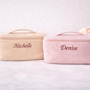 Puede incluir: Dos neceseres de pana, uno beige y otro rosa, cada uno con asa y nombre bordado. La bolsa beige dice "Michelle" y la rosa dice "Denise". Las bolsas son rectangulares con cierre de cremallera.