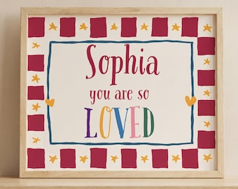 Könnte beinhalten: Ein rechteckiger gerahmter Druck mit dem Namen Sophia und dem Text you are so LOVED in bunter Schrift. Der Rand besteht aus abwechselnden dunkelroten Quadraten und kleinen gelben Sternen auf cremefarbenem Grund mit einer dunkelblauen Umrandung.