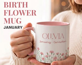 Könnte beinhalten: Ein weißer Keramikbecher mit rosafarbenem Innenraum und Henkel, der den Namen OLLVIA in rosa Schrift über den Wörtern January Carnation sowie eine untere Bordüre aus rosa Nelkenblüten mit grünen Stielen und Blättern auf der Vorderseite zeigt.