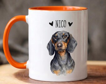 May include: A white ceramic mug with a bright orange handle and interior rim. The front features a watercolor-style illustration of a black and tan dachshund dog centered below the name NICO in black text, flanked by two small black heart icons.