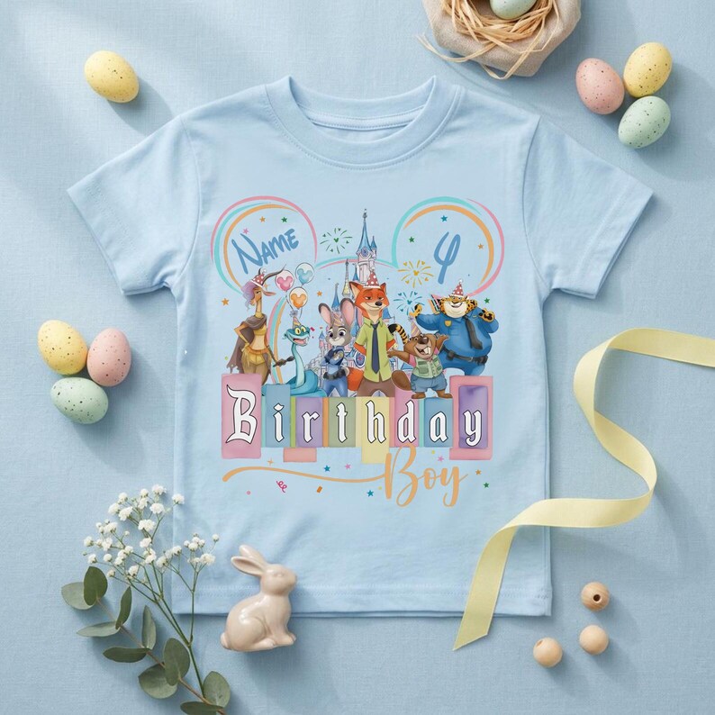 Pu&ograve; includere: Una t-shirt a maniche corte color azzurro con una grafica colorata di personaggi animali animati che indossano cappellini da festa, la sagoma di un castello e il testo Name, 4 e Birthday Boy in un carattere giocoso, centrato sul davanti.