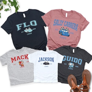 May include: Five short-sleeved t-shirts in various colors, each featuring a different name and a cartoon car graphic. The shirts include the names "FLO", "SALLY CARRERA", "MACK", "JACKSON", and "GUIDO", with "CARS" and the year "2006" also printed.
