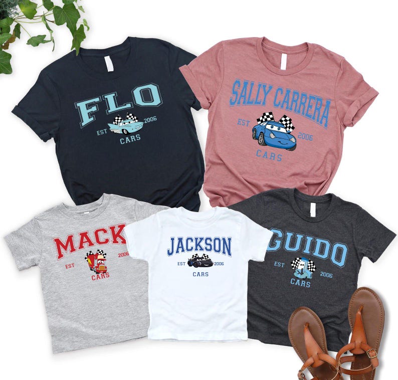 May include: Five short-sleeved t-shirts in various colors, each featuring a different name and a cartoon car graphic. The shirts include the names "FLO", "SALLY CARRERA", "MACK", "JACKSON", and "GUIDO", with "CARS" and the year "2006" also printed.