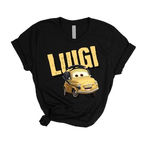 May include: Black t-shirt featuring the name "Luigi" in yellow block letters above a cartoon image of a yellow car with headphones. The car has a smiling face and is from the movie "Cars".