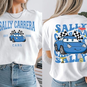 May include: White t-shirt featuring a blue cartoon car with the text "SALLY CARRERA" and "CARS" in blue. The front design includes a checkered flag and the text "EST. 2006". The back of the shirt has a similar design with additional text and a Route 66 symbol.