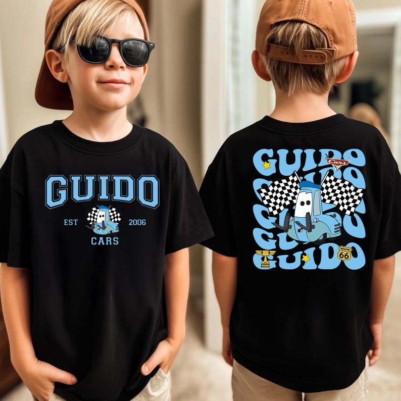 May include: Black t-shirt featuring the name "GUIDO" in light blue, with a cartoon car and checkered flag design. The shirt also includes the text "EST 2006 CARS". The back of the shirt has a similar design with the name "GUIDO" and a cartoon car.