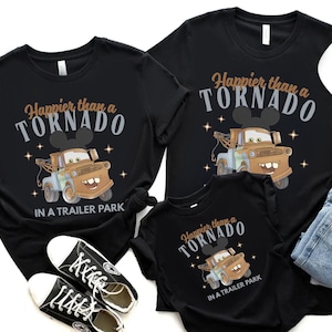Puede incluir: Camisetas negras con la frase "Happier than a Tornado in a Trailer Park" y un dise&ntilde;o de cami&oacute;n de remolque de dibujos animados. La imagen incluye vaqueros y zapatillas negras.