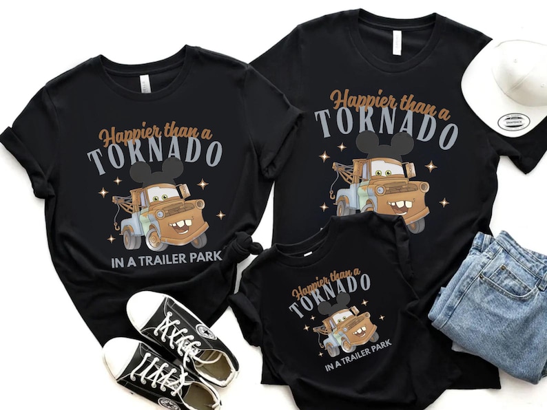 Puede incluir: Camisetas negras con la frase "Happier than a Tornado in a Trailer Park" y un dise&ntilde;o de cami&oacute;n de remolque de dibujos animados. La imagen incluye vaqueros y zapatillas negras.