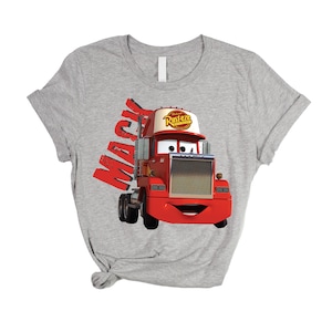 May include: A gray t-shirt featuring a cartoon image of Mack, the red semi-truck from the movie Cars. The word "Mack" is printed in red on the left side of the shirt. The truck has a white and red hat that says "Rusteze".