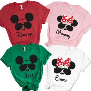 K&ouml;nnte beinhalten: Vier kurz&auml;rmelige T-Shirts in Rot, Rosa, Gr&uuml;n und Wei&szlig;. Jedes Shirt zeigt ein Cartoon-Mausgesicht mit Sonnenbrille. Das rote Shirt sagt "Daddy", das rosa Shirt sagt "Mommy", das gr&uuml;ne Shirt sagt "Jake" und das wei&szlig;e Shirt sagt "Emma".