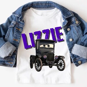 May include: White t-shirt featuring a cartoon black car with the name "LIZZIE" in purple letters. The shirt is paired with a blue denim jacket. The car has large eyes and a friendly expression. The overall theme is children's apparel.