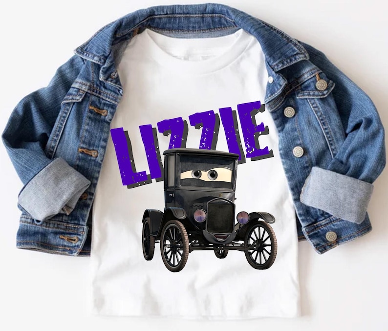 May include: White t-shirt featuring a cartoon black car with the name "LIZZIE" in purple letters. The shirt is paired with a blue denim jacket. The car has large eyes and a friendly expression. The overall theme is children's apparel.