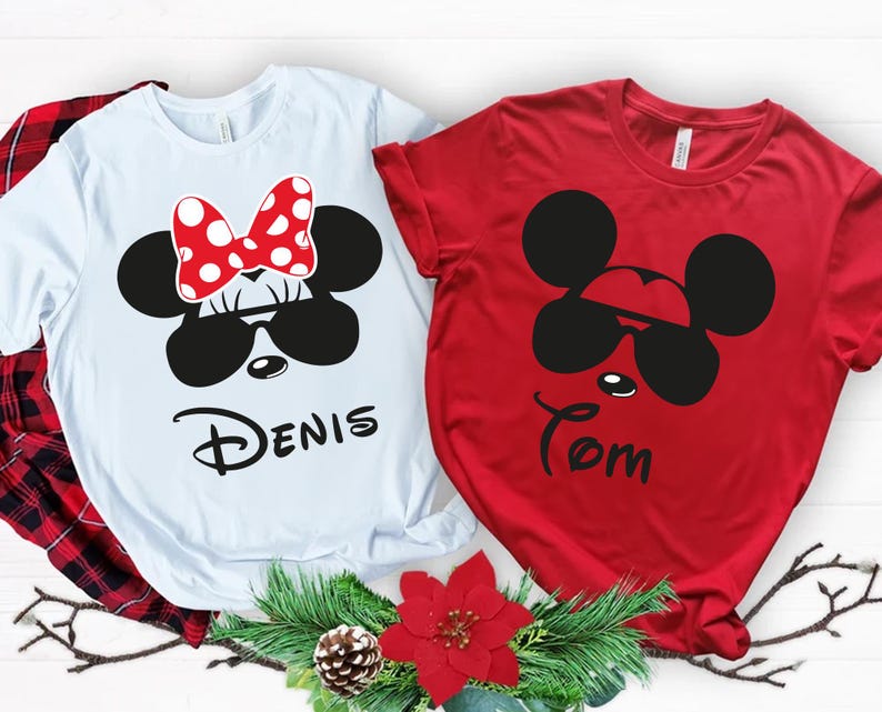 K&ouml;nnte beinhalten: Zwei kurz&auml;rmelige T-Shirts, eines wei&szlig; und eines rot, mit Cartoon-Mausgesichtern mit Sonnenbrillen. Das wei&szlig;e Shirt hat eine rote Schleife mit Punkten und den Namen "Denis". Das rote Shirt hat den Namen "Tom".