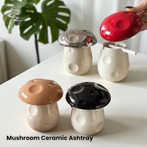 May include: A collection of mushroom-shaped ceramic ashtrays in various colors: brown, black, silver, and red. The ashtrays have a cream-colored base with a textured cap. The text "Mushroom Ceramic Ashtray" is at the bottom.