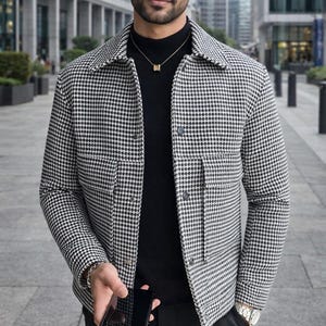 May include: A black and white houndstooth jacket with a collared neckline and two front pockets. The jacket is worn over a black turtleneck. The image includes the text "REALEVER". The person is holding a smartphone.