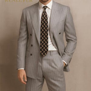 May include: A light gray double-breasted suit with vertical pinstripes. The suit is paired with a white dress shirt and a black tie with a paisley pattern. The image includes the text "Look iconic with REALEVER".