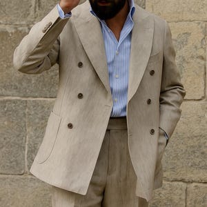 May include: A beige linen suit with a double-breasted jacket and matching trousers. The jacket has dark brown buttons and a notched lapel. A light blue striped shirt is worn underneath. The text "Look Iconic with REALEVER" is visible.