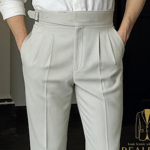 May include: Light gray pleated trousers with a matching belt, paired with black leather dress shoes. The pants have a tailored fit and are worn with a white shirt. The image includes the text "Look Iconic with REALEVER".