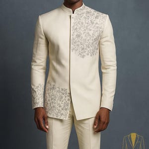 May include: Ivory suit with intricate silver embroidery on the jacket's front and sleeves. The suit features a mandarin collar and tailored trousers. The image also includes brown leather shoes. The text in the image says "Look Iconic with REALEVER".