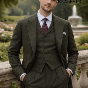 May include: A three-piece olive green suit with a white dress shirt and patterned burgundy tie. The suit includes a blazer, vest, and pleated trousers. The image includes the text "Look iconic with REALEVER".