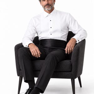 May include: A white tuxedo shirt with a pleated front and black buttons, paired with a black cummerbund and black trousers. The shirt features long sleeves with French cuffs and black cufflinks. The brand name REALEVER is printed at the top.
