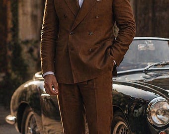 May include: A brown double-breasted suit with a white and blue striped shirt and a pocket square. The suit is paired with brown loafers. The image includes the text "Look Iconic with REALEVER" and the REALEVER logo.