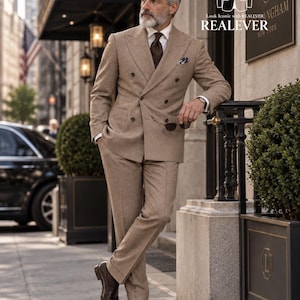 May include: A tan double-breasted suit with a white collared shirt, a dark brown tie, and a pocket square. The suit features a textured fabric, peak lapels, and dark buttons. The text "Look Iconic with REALEVER" is visible in the upper right corner.