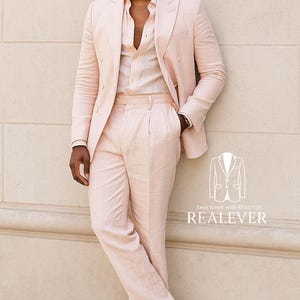 May include: A light pink linen suit, including a double-breasted blazer and matching trousers, paired with a light pink button-down shirt. The outfit is completed with white sandals. The image includes the text "Look Iconic with REALEVER" and the brand name.
