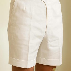 May include: White shorts with a tailored design. The shorts feature a button closure, belt loops, and folded cuffs. The fabric appears to be a lightweight material, suitable for warm weather. The shorts are part of a clothing collection.