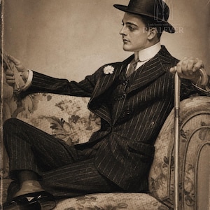 May include: A sepia-toned portrait of a person wearing a dark pinstriped suit, a white detachable collar, a tie, and a bowler hat. A small white flower is pinned to the lapel. The person holds a cane and a pair of gloves in a seated position.
