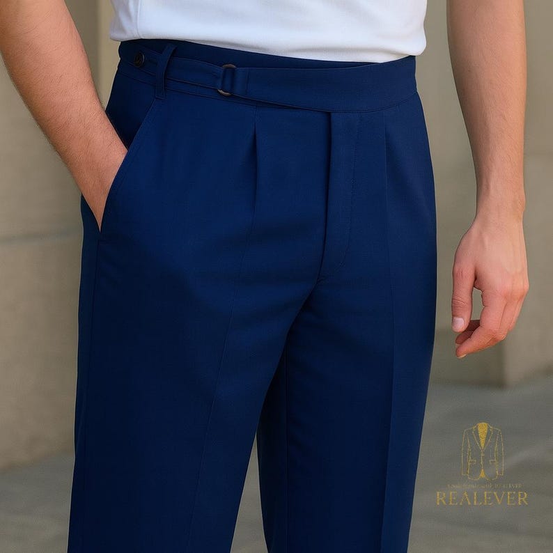 May include: Close-up of navy blue trousers with a belt and pleats. The trousers have a tailored fit and a classic design. The person is wearing a white shirt. The image is well-lit, highlighting the fabric and details of the pants.