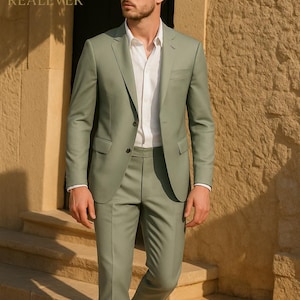 May include: A light green suit with a white dress shirt. The suit includes a blazer and matching trousers. The image also shows a pair of brown shoes and sunglasses. The text "REALEVER" is visible.