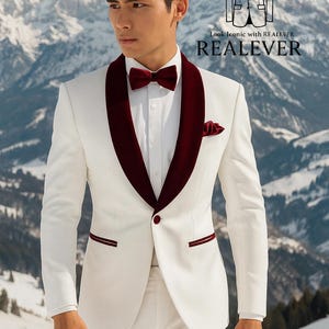 May include: A white suit with a burgundy velvet lapel, bow tie, and pocket square. The suit has a single-button closure and burgundy trim on the pockets. The text "Look Iconic with REALEVER" is visible in the background.