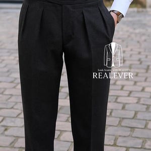 May include: Dark gray pleated trousers with a high waist. The pants have a tailored fit and a classic design. The text "REALEVER" is visible on the lower right. A white shirt and a watch are also visible.