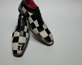 May include: A pair of black and white checkered dress shoes with black laces. The shoes have a glossy finish and a red sole. The shoes are displayed on a white background.