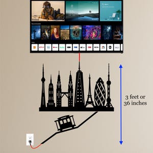Puede incluir: Arte mural de silueta negra que representa paisajes urbanos y un teleférico, con un cable rojo que va a una toma de corriente. El arte mide aproximadamente 91 cm de alto. Una pantalla de TV está montada encima.