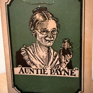 May include: A vintage-style rectangular cardboard box featuring a green central panel with a black and white illustration of a person wearing glasses and holding a small jar. The text "AUNTIE PAYNE" is printed below, with "RMFUL DRUGS - MENTHOL, CAMPHOR" at the bottom.