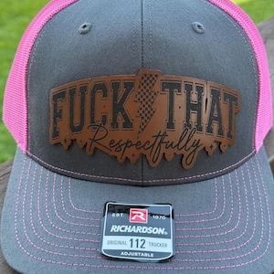 May include: A gray Richardson 112 trucker hat with a pink mesh back and brim stitching. The hat features a brown leather patch with the words "FUCK THAT Respectfully" and a lightning bolt graphic.