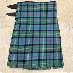 Könnte beinhalten: Ein grüner, blauer und schwarzer Schottenkilt mit zwei schwarzen Lederriemen. Der Kilt zeigt ein klassisches Tartanmuster mit roten Akzenten. Der Stoff ist gefaltet und betont das Webdesign. Ein traditionelles Kleidungsstück.